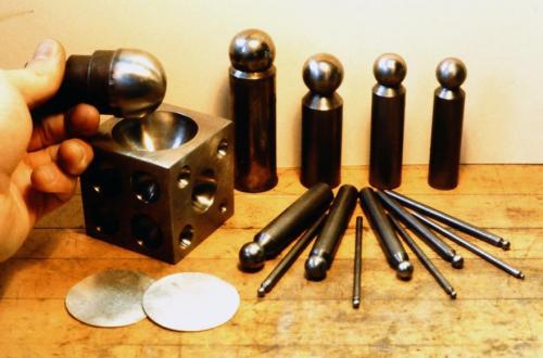 A dapping block with half-spherical holes, domed steel punches, and two sterling circles used to make the spherical transition in the design.