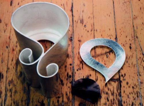 The basic form of the pitcher is complete. The agate is cut and polished. A base is soldered into the pitcher with a "window" for the agate. A second frame, the same shape as the base, is also shown. This will fit the outer surface of the agate and eventually hold it in place.