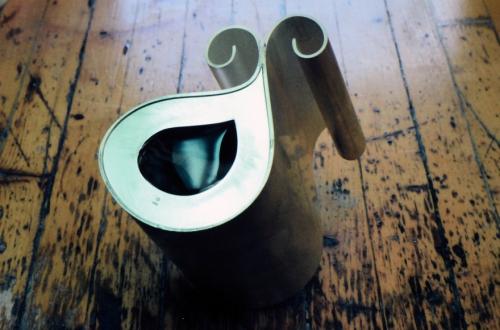 The agate and second frame are precisely seated together and shown in place. The outer edge of the frame is bevelled, and the bottom edge of the vessel itself serves as a bezel. The stone held by the frame will be set as a unit. Also, prior to this, the pitcher's pouring spout shapes will be gently flared.