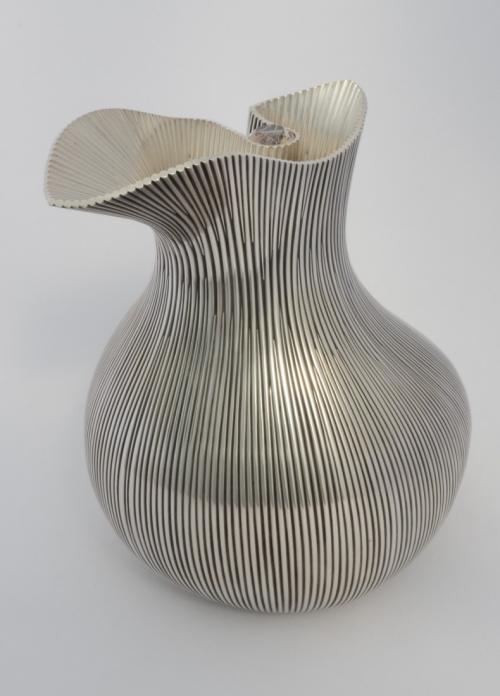 The finished pitcher. The surfaces have been polished and the grooves on the outer surface have been oxidized. A facetted rutillated quartz is set in the curve above the handle area.