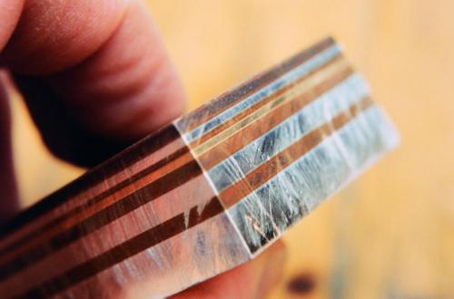 The fused stack. The layers were bolted between steel plates under hydraulic pressure. The assembly of bolted steel and mokume stack was embedded in charcoal inside a sealed stainless steel foil bag (to create a reducing or non-oxidizing atmosphere). The stainless steel bag and its contents were heated in a digital kiln for 14 hours at a temperature just below the melting point of any eutectic alloy between the layers (about 1400 degrees fahrenheit.). Under these conditions, molecular growth between the lay