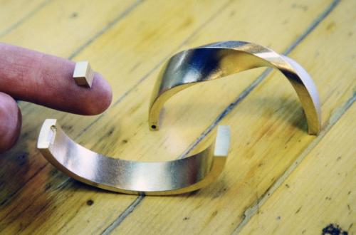The bracelet is cut exactly in half at the places that will become its hinge and catch. A rectangular block of gold (on my finger) is shown prior to being soldered into one end as part of the hinge.