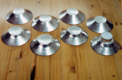 The four holders in the back now have about 3 courses. During the raising process, a mechanical advantage achieved over the metal gradually constricts the overall circumference of the disk (a thickening process) while, at the same time, the metal is pinched between steel (a thinning process). The top area of the four holders shown in the front row are beginning to be worked into a curved contour.