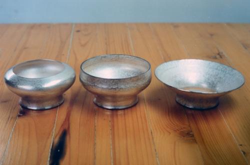 Three holders seen at three stages of completion (from right to left). This photograph clearly shows the progression of constricting the outer circumference in upon itself. Very gradually, and with frequent annealing, the metal literally flows as a plastic solid. Each course is necessarily a tiny approximation toward a goal.