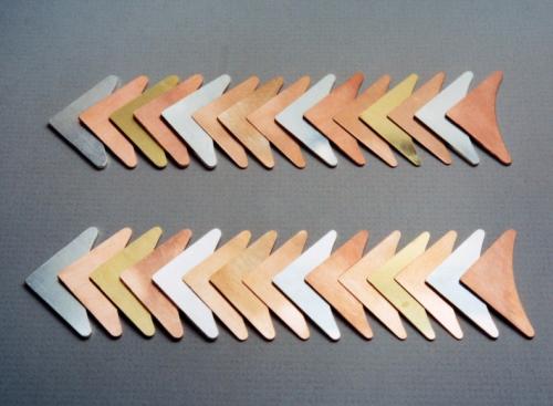 Two rows of fifteen layers of different coloured metals, all perfectly flat and clean. A layer of 18 k. green gold is seen fourth from the right in each row. The other metals are sterling silver, copper, brass, and two copper alloys: shakudo, and shibuichi.