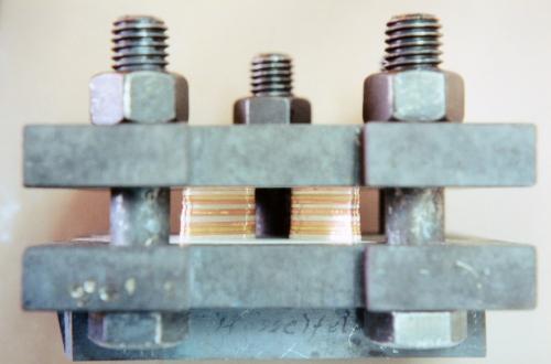 The two sets of fifteen layers are stacked and bolted tight between steel plates under hydraulic pressure.