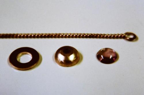 From left to right: the table for the stone (with hole), the domed disc (formed in a steel dapping block with hemispherical shaped depressions) that will become the leaves, the pink tourmaline and, behind these, the twisted wire.