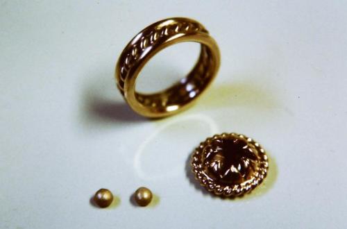 The ring shank is soldered together and joined. The leaves and table and stone are seen nested together. Two decorative spheres have been formed by melting scraps of red gold such that they bead up into balls.