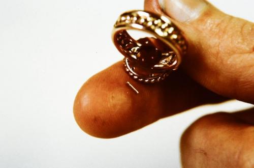 The underside of the leaves and circle of twisted wire is shaped to precisely fit over the table at the same time as it holds the stone down to the table. Then, four small rivet holes are drilled (three of these can be seen) and four little rivet wires are made (one of these is seen on my finger tip). The entire piece is pre-polished and the four rivets are set, locking together the entire assembly.