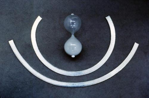 The two sterling rods are shown at different stages of being forged into circles. A cross-peen hammer, with its oval or rounded rectangular hammer head, is struck perpendicular to the length of the rod. The outer edge of the curve is hammered more than the inside edge thus pinching/flowing that edge more and causing the rod to steer in a curve.