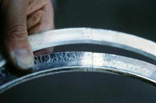 The ends of the forged circles are lap-joined for strength. The join in the background has been soldered. The join in the foreground (not yet soldered) shows the overlapping ends and also shows the heads of two rivets that pre-lock and tighten the join in preparation to be soldered.