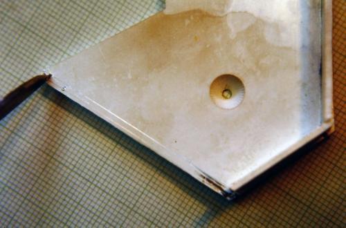 Two parallel scribed lines can be seen where the fifth wall will be soldered. The inner line was scratched along the edge of the labradorite, and the outer line was similarly scratched along a sterling wall temporarily pressed against the side of the stone. The tool at the top of the photo is an engraver. Precisely along both lines, little engraved stitches are being curled up which will locate and lock the wall in place during the soldering. Note also that the hole for the citrine in its cylinder is only p