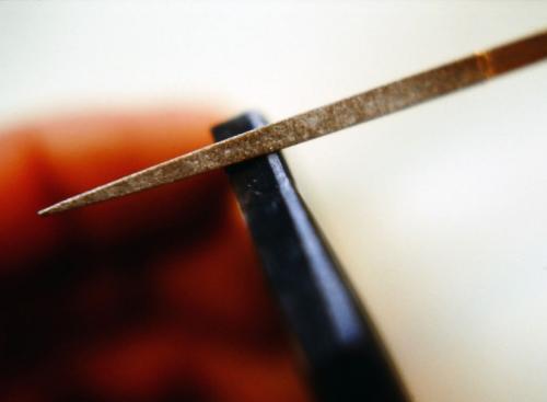 The next stage is to set the stone. Here the upper millimeter or so of the labradorite's vertical edge is slightly beveled with a diamond file (the light angle in the photo). Each file stroke is directed from right to left toward the back of the stone (as seen in this photo) to avoid any chipping up along front edges. The top of the metal "walls" will be pressed/ folded over to this beveled edge to secure the stone.
