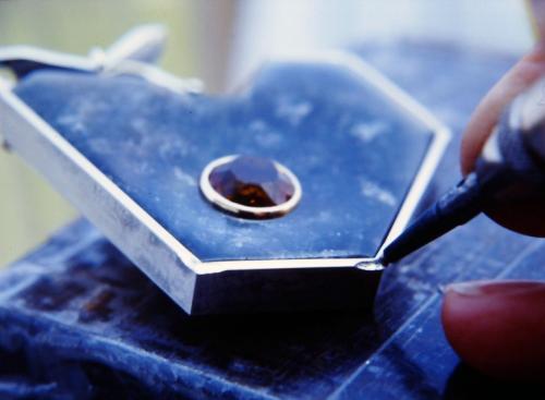 The setting tool used is the Foredom attachment that works like a miniature jack-hammer. This photo shows the placement and angle at which the tool moves the metal. When worked at this angle, the metal closest to the stone remains smooth. The corner areas of the wall are worked first. The metal literally flows across toward the stone while also folding along the undercut. Extreme care is taken to move the metal only to the stone and no further (labradorite will instantly bruise and chip if pinched).